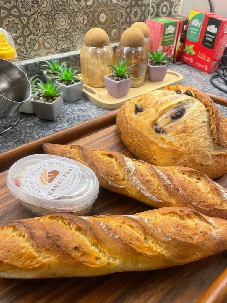 Kamal Bake artisan baguettes and sourdough boule on a wooden tray with branded packaging
